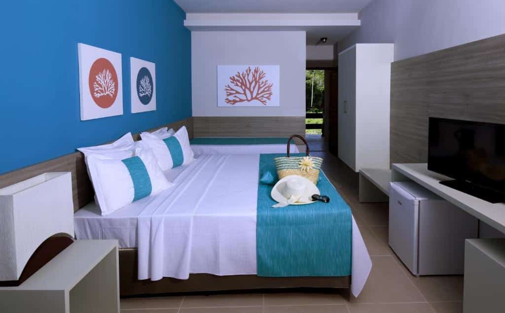 Quarto moderno do Tabaobí Smart Hotel com cama de casal, parede com detalhes em azul, TV, frigobar e decoração com tema de praia.