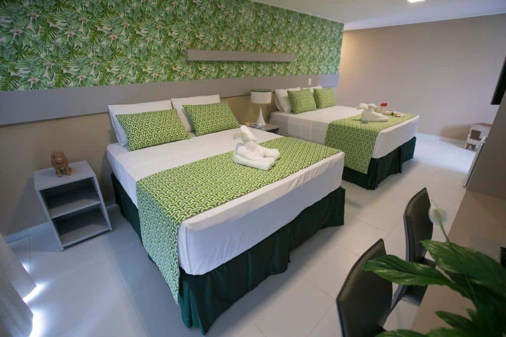 Quarto do Baía Branca Hotel com duas camas de casal, roupa de cama com estampa verde, mesas de cabeceira, luminárias e uma parede com detalhes florais.