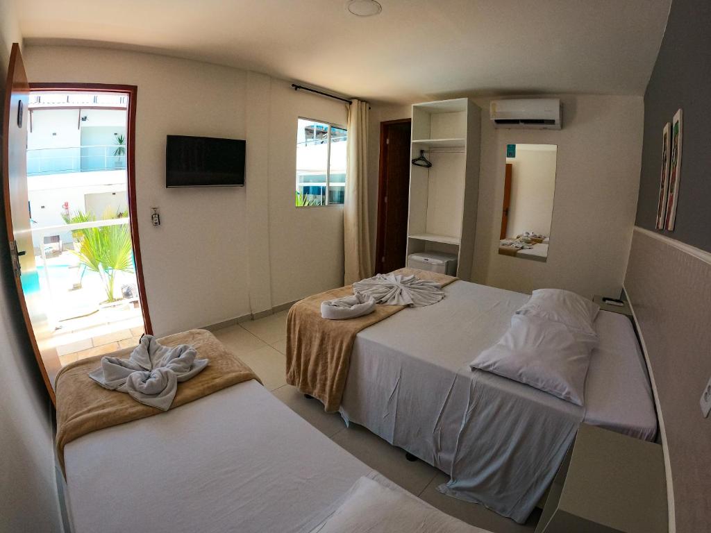 Quarto do Vila de Maré Hotel com duas camas, TV, armário aberto, espelho, toalhas em formato de cisnes e uma janela com vista para a piscina externa.