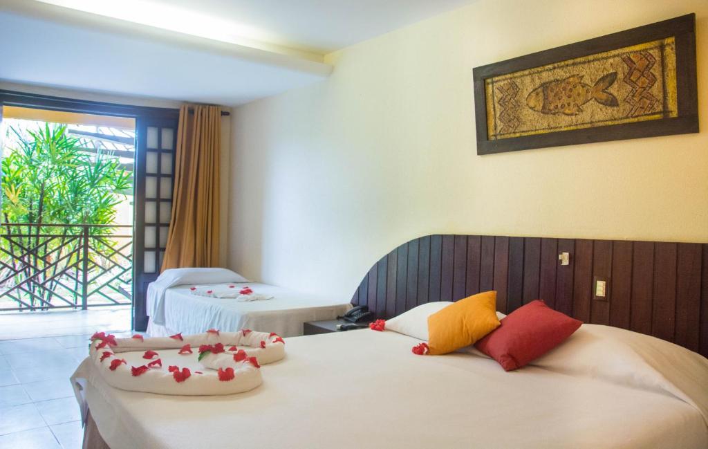 Quarto do Hotel Aconchego com uma cama de casal e uma cama de solteiro, ambas decoradas com pétalas de rosa; varanda com plantas visíveis.