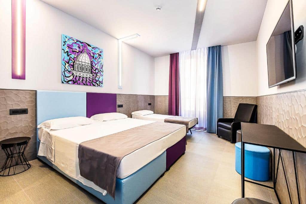 Quarto do Hotel Relais Dei Papi moderno com duas camas, uma TV na parede, uma escrivaninha, uma cadeira, cortinas coloridas e obras de arte.