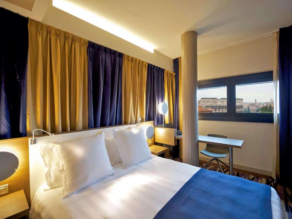 Um quarto do Mercure Roma Centro Colosseo com uma cama de casal, cortinas azuis e douradas, uma pequena escrivaninha e uma janela com vista para a cidade.