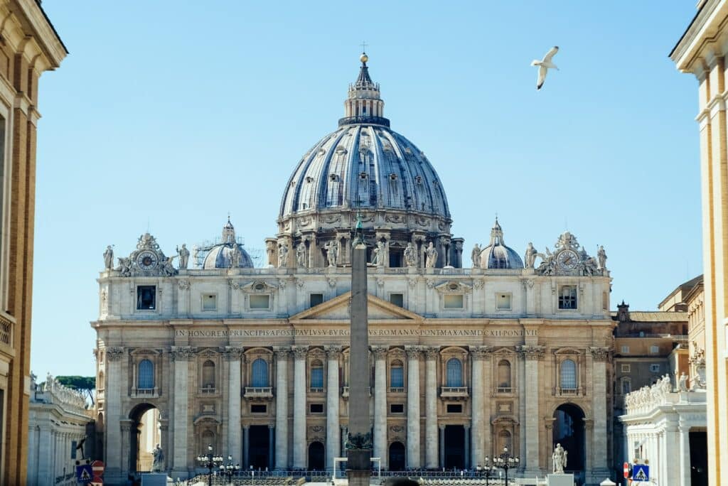 Basílica de São Pedro na Cidade do Vaticano com uma cúpula central, um obelisco na frente e uma gaivota voando acima.