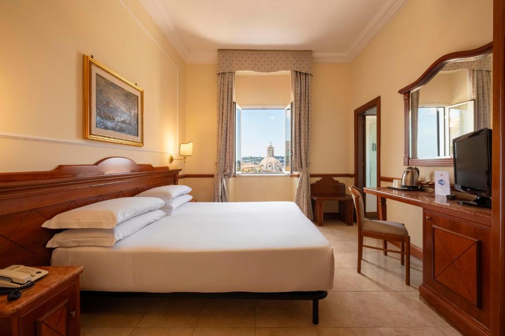 Um quarto do Hotel Hiberia com uma cama de casal, escrivaninha, TV, espelho, chaleira e uma janela com uma paisagem urbana do lado de fora.