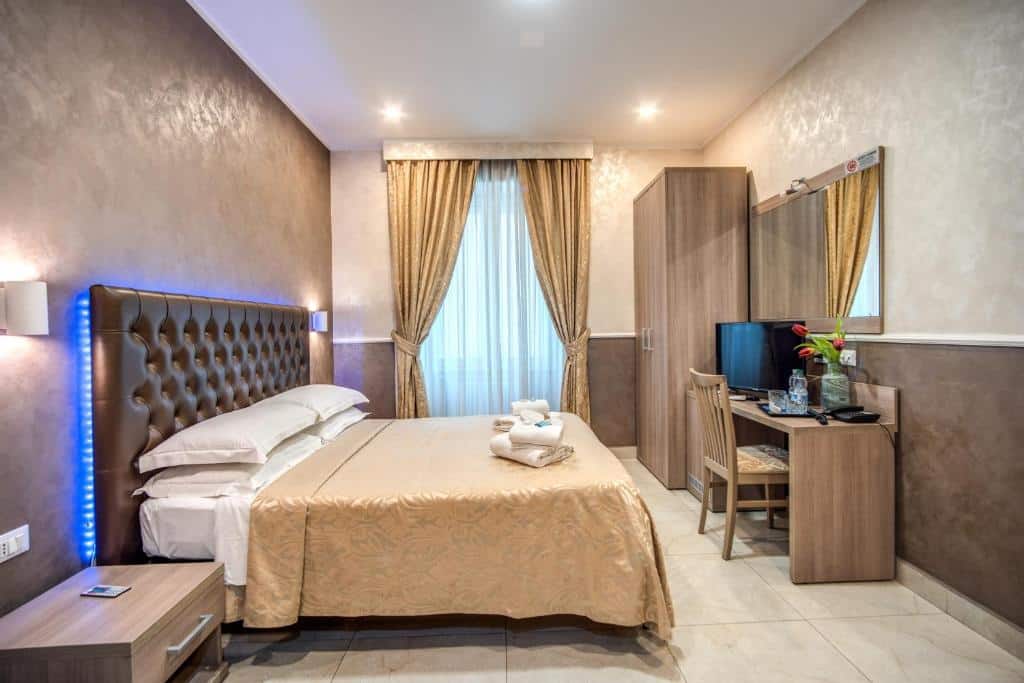 Quarto do Hotel Centro Cavour Roma com uma cama de casal, criado-mudo, guarda-roupa grande, escrivaninha com cadeira, TV, espelho e janela com cortinas douradas.