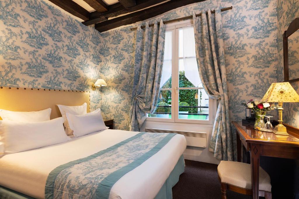 Quarto do Relais Hôtel du Vieux Paris, um dos hotéis em Saint Germain em Paris. Uma cama de casal está encostada na parede esquerda do local com mesinhas de cabeceira e abajures dos dois lados. Logo em frente fica uma mesa com banquinho, abajur, vaso de flores e cafeteira. Na lateral esquerda há uma janela com cortinas.