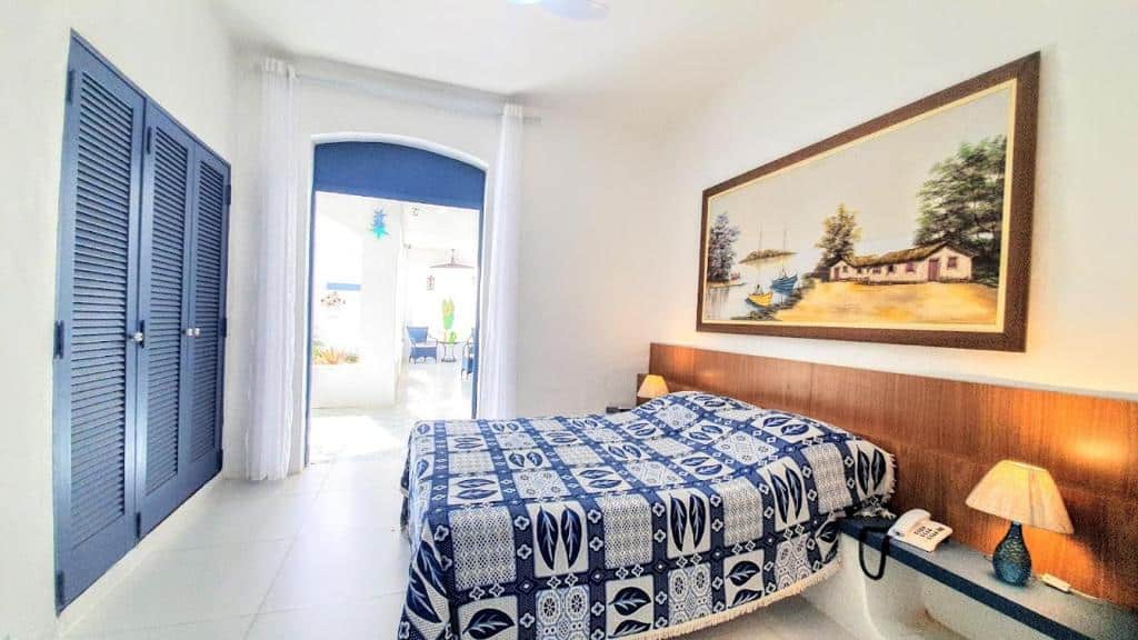 Quarto do Brisa do Mar Barê Praia Hotel com cama de casal do lado direito da imagem no centro do quarto em cada lado da cama uma cômoda com luminária. Representa hotéis em São Sebastião.