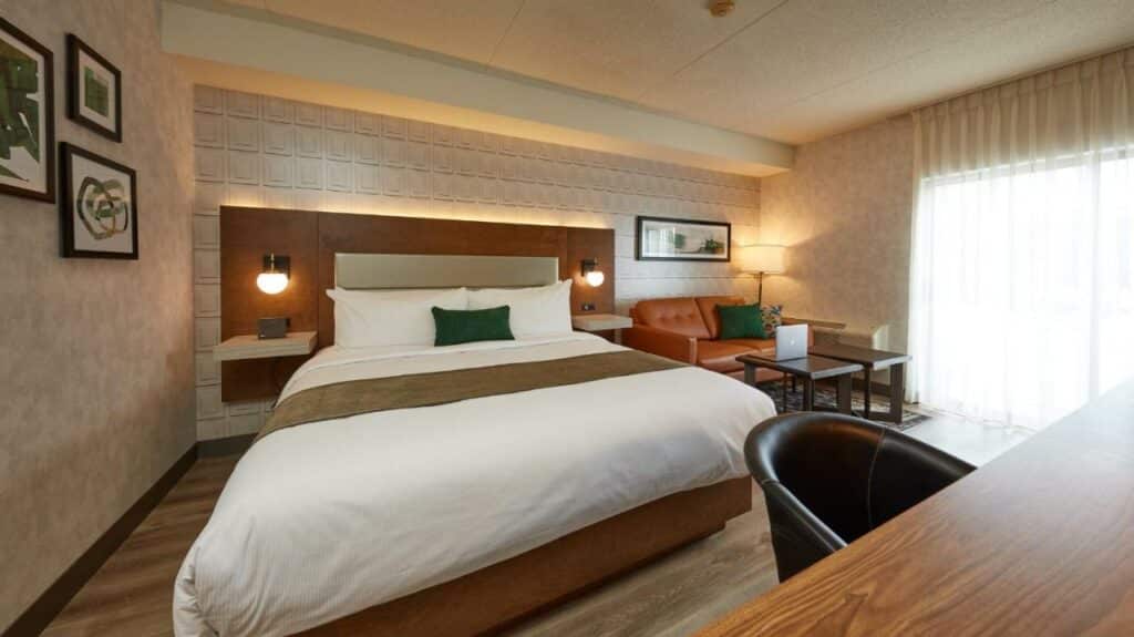 Quarto amplo no Stay Inn Hotel Toronto, com um sofá de couro, uma mesinha de centro, uma varanda, uma cama de casal, um poltrona, tudo em tons de bege, caramelo e marrom