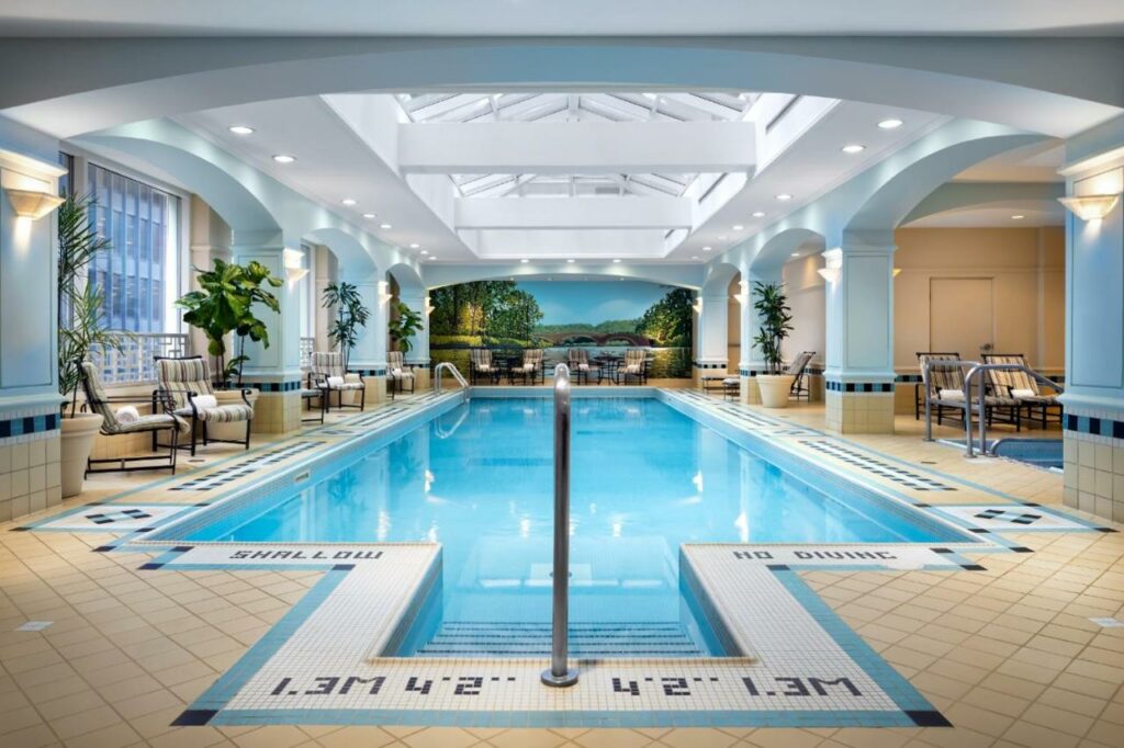 Piscina ampla e coberta no Fairmont Royal York Gold Experience, com janelas, cadeiras e vasos de flor ao redor