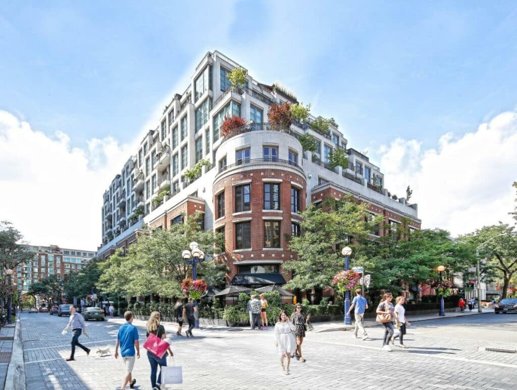 Prédio do The Hazelton Hotel que ocupa uma esquina, tem diversos andares, muitas janelas, numa rua movimentada e cercado por árvores
