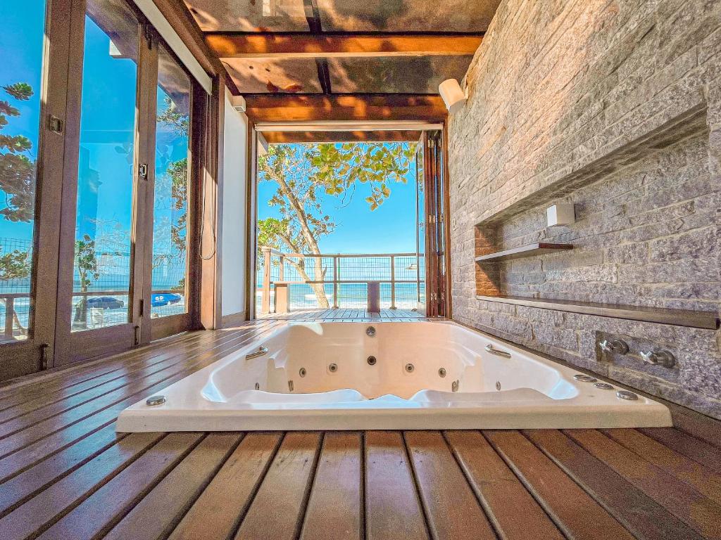 Uma jacuzzi interna iluminada pelo sol do hotel Nacional Inn Ubatuba. Ela está situada em um piso de madeira, com grandes janelas e vista para as árvores e o oceano do lado de fora.