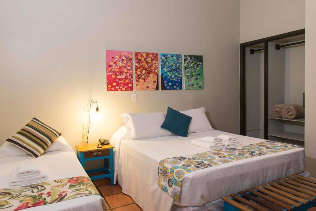Quarto do Hotel Porto di Mare, com uma cama de casal e uma cama de solteiro, além de uma mesinha de cabeceira entre as duas camas, e um armário aberto ao fundo