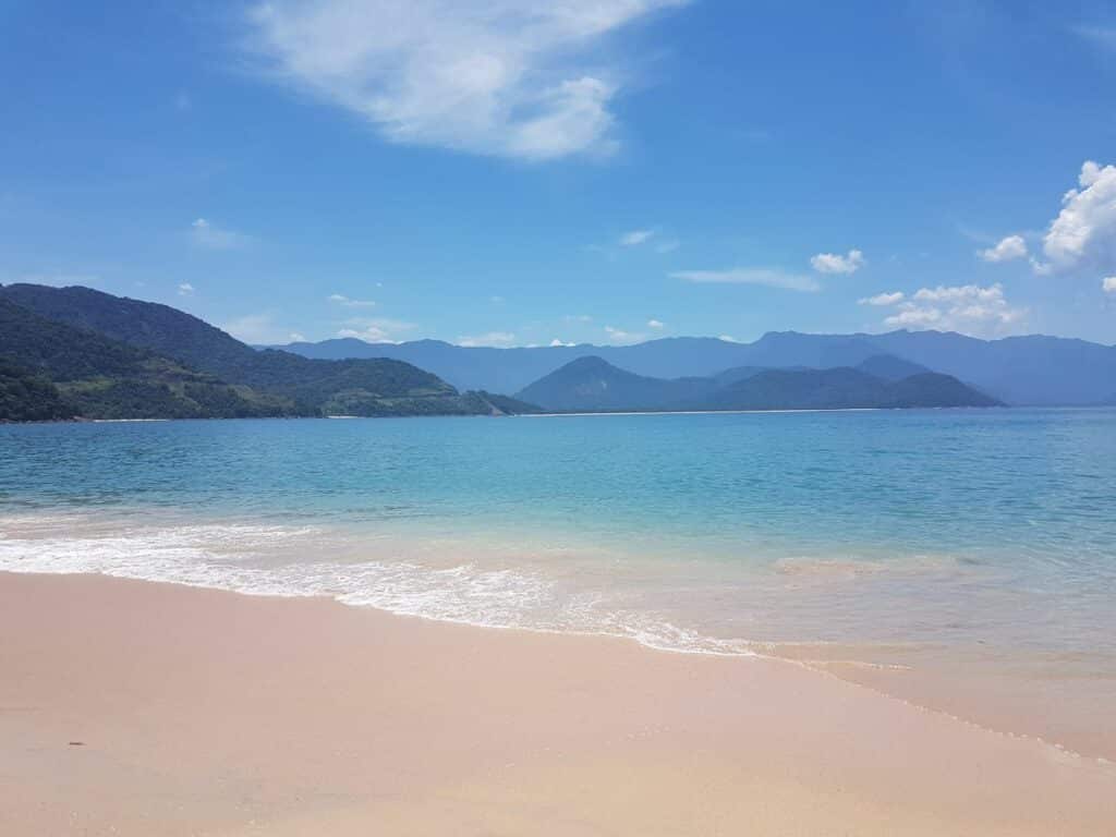 Mar turquesa com vista da Ilha do Prumirim, em Ubatuba, em dia de céu azul com nuvens esparsas