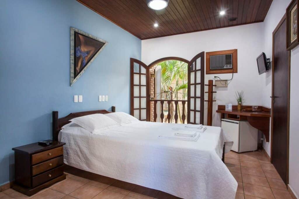 Quarto do Giprita Wellness Hotel Ubatuba, um dos hotéis em Ubatuba, com uma pequena TV na parede, frigobar, ar-condicionado antigo e cama de casal