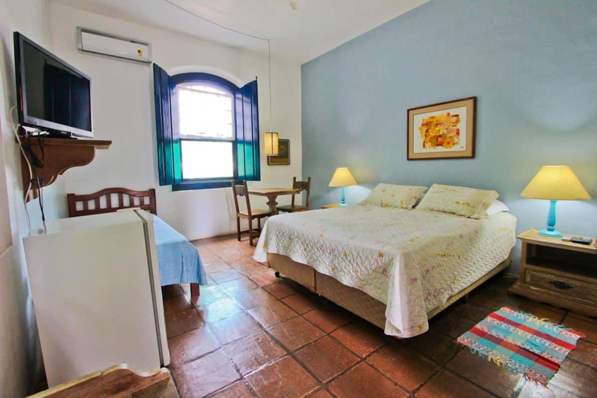 Quarto do Hotel Solar das Águas Cantantes, na Praia do Lázaro, em Ubatuba, com cama de casal, mesinhas de cabeceira com abajures, ar-condicionado e TV