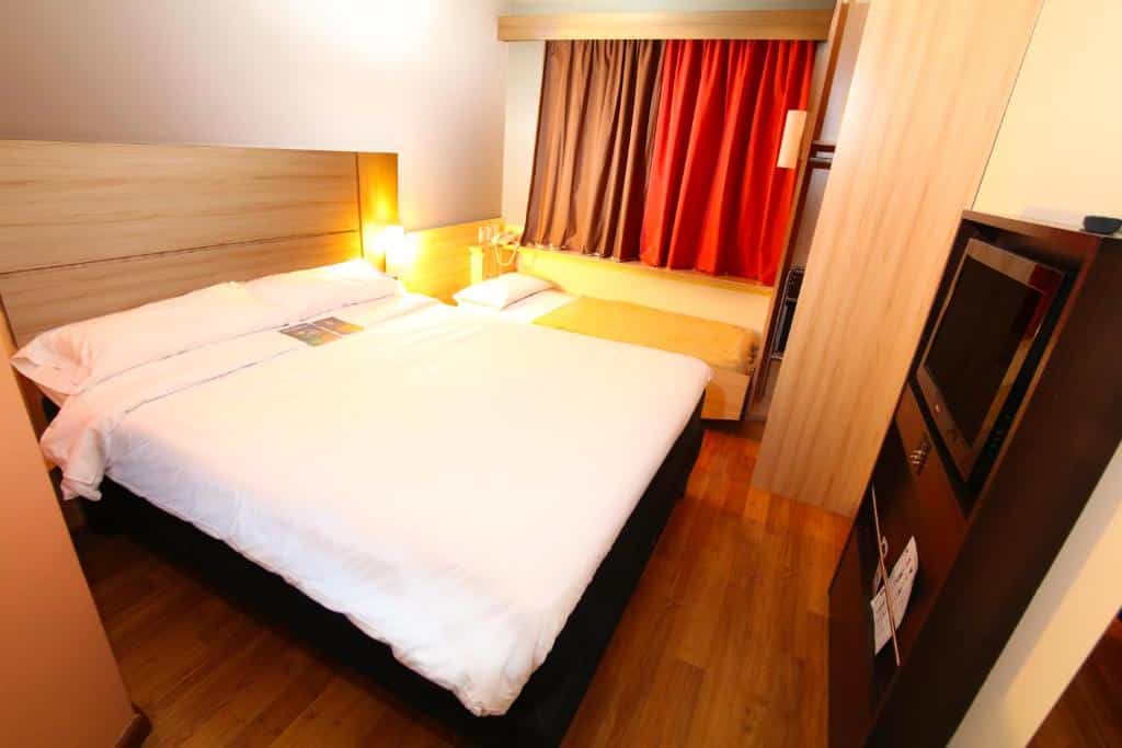 Quarto do ibis Santiago Providencia com uma janela com cortinas, uma cama de casal e uma cama menor de solteiro, um pequeno armário e uma televisão