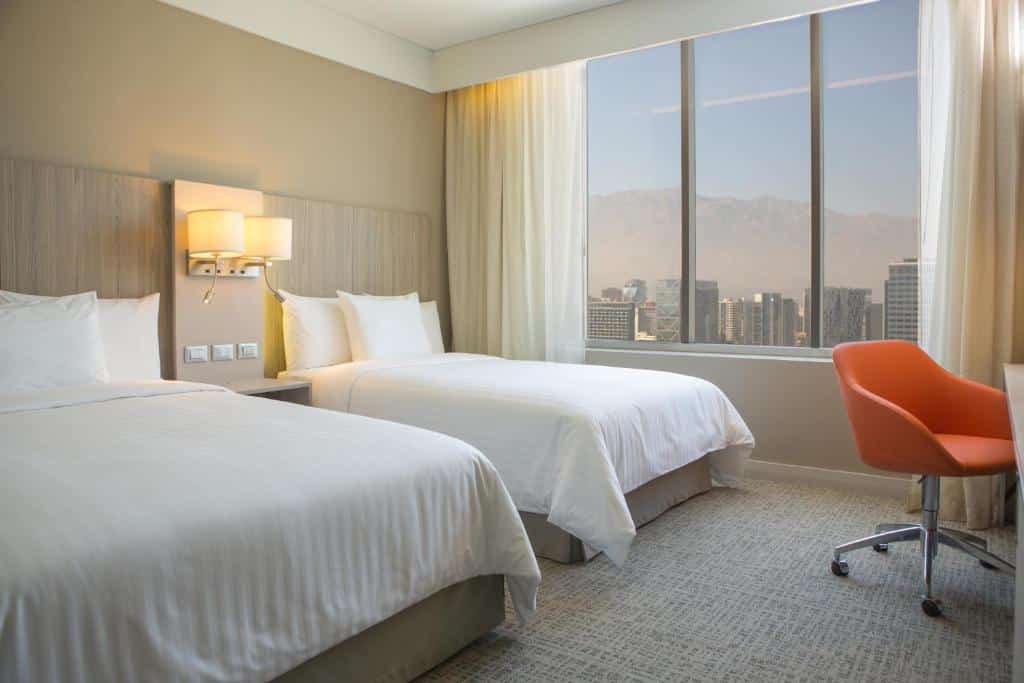 Quarto do Courtyard by Marriott Santiago Las Condes com duas camas de solteiro do lado esquerdo uma mesa de trabalho em frente as camas.