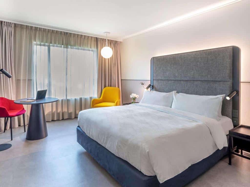 Quarto do Pullman Santiago Vitacura com cama de casal do lado direito, uma poltrona amarela do lado esquerdo da cama. 