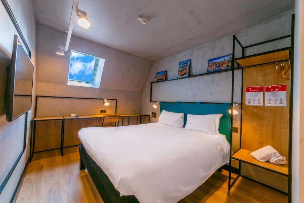 Quarto do ibis Porto Centro Mercado Bolhao com cama de casal do lado direito da imagem, em frente a cama uma TV presa na parede e do lado esquerdo da cama uma mesa de trabalho com cadeira. Representa hotéis Mercure no Porto.