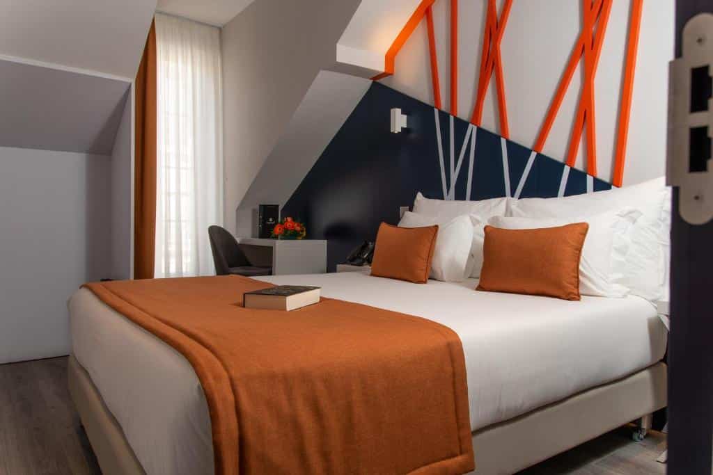 Quarto do Be Poet Baixa Hotel com uma cama de casal, uma janela com cortina do lado esquerdo, próximo há uma mesa de escritório com uma cadeira, para representar hotéis no centro de Lisboa.