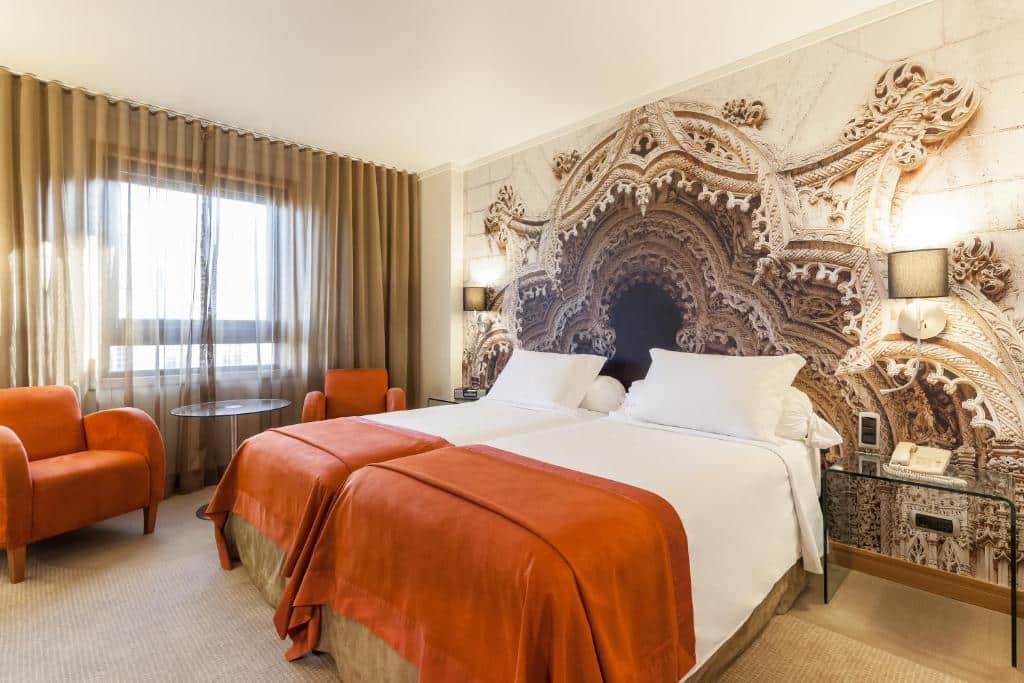 Quarto do Hotel Marques De Pombal com duas camas de solteiro, do lado esquerdo do quarto há uma janela com cortinas, embaixo dela há duas poltronas e uma mesinha redonda, para representar hotéis no centro de Lisboa.