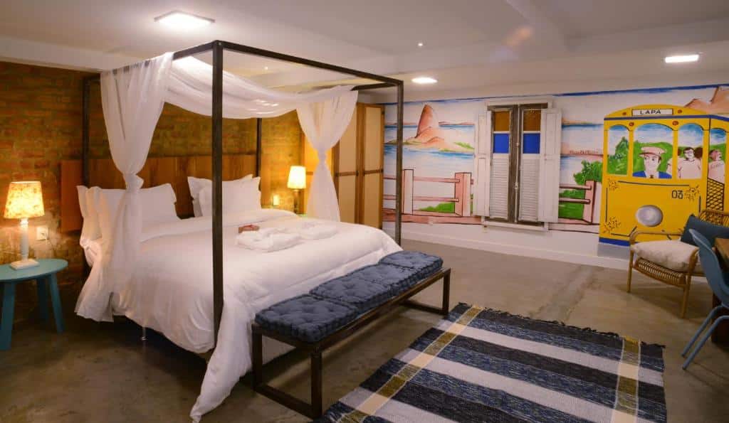 Um quarto com uma cama de dossel, mesas de cabeceira, um banco, um tapete e um mural de um bonde e uma janela na parede.