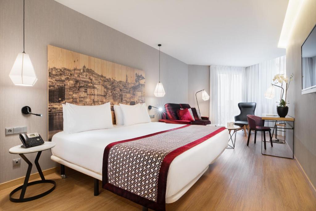 Quarto moderno no Eurostars Porto Centro com uma cama grande, mesas de cabeceira, uma escrivaninha, poltrona e arte de parede de paisagem urbana, para representar hotéis no Porto em Portugal.