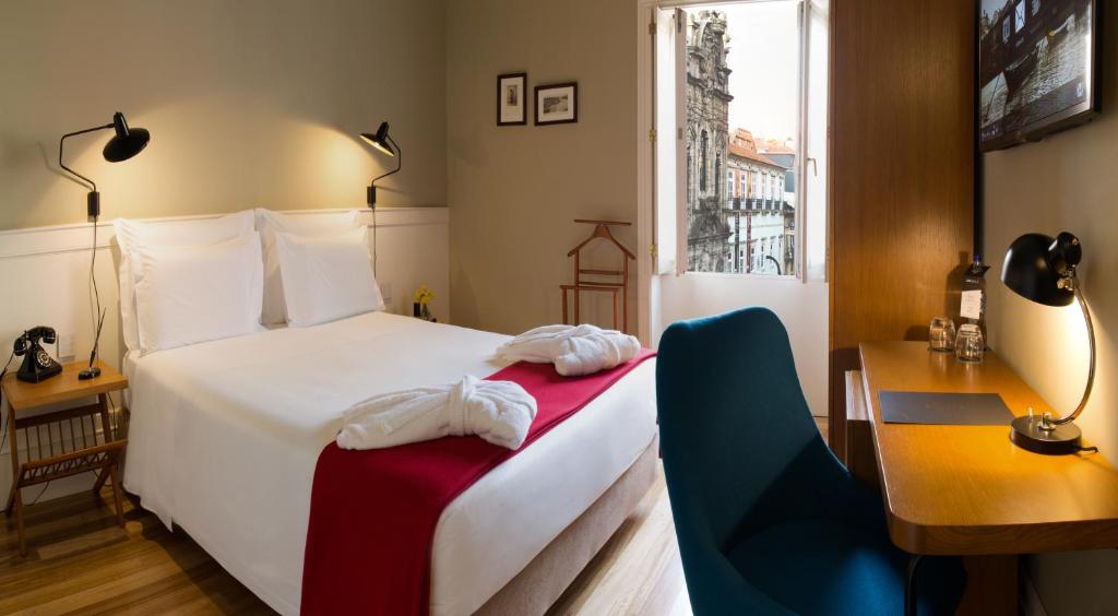 Quarto no Porto A.S. 1829 Hotel com cama de casal, escrivaninha, cadeira, TV e janela aberta mostrando os prédios do lado de fora; cobertor vermelho na cama, para representar hotéis no Porto em Portugal.