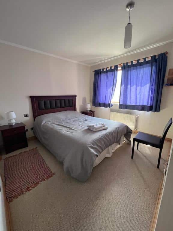 Quarto do Dúplex En Valle Nevado 6PAX, Valle de Cóndores II Servicio HOM com cama de casal do lado esquerdo com duas cômodas de madeiras com luminária. 