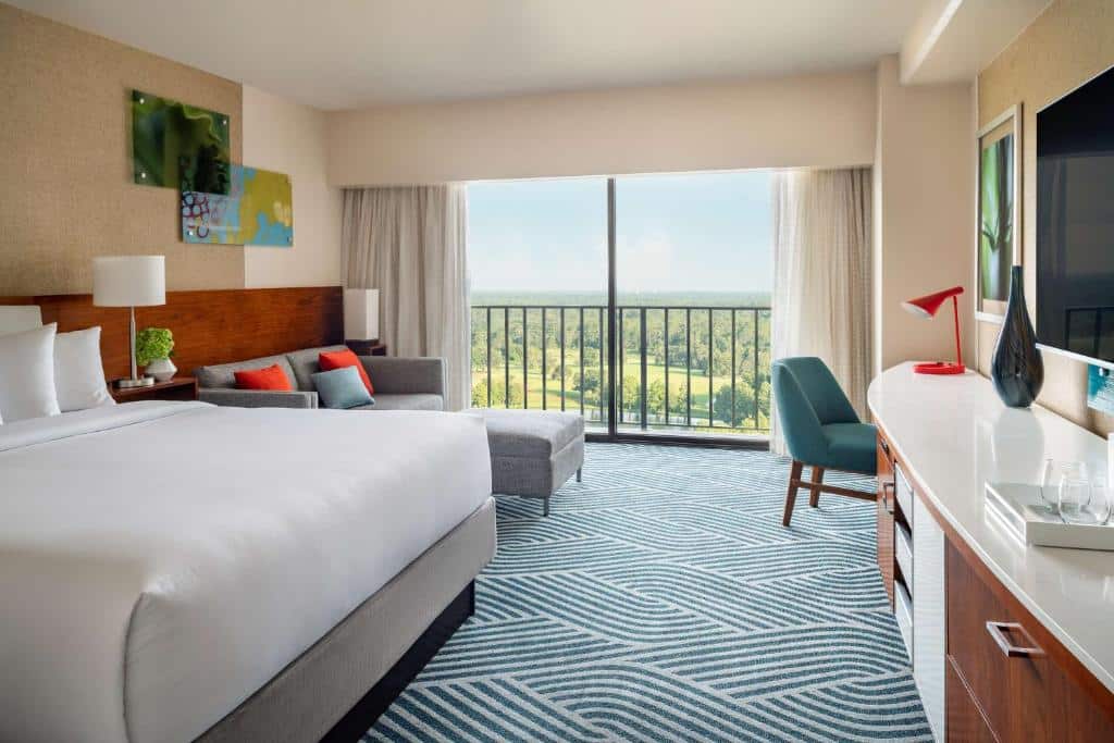 quarto com varanda e vista do Hyatt Regency Grand Cypress Resort em um ambiente amplo com cômoda, tv e bancada com cadeira e cores alegres em frente à uma cama de casal com um sofá ao lado