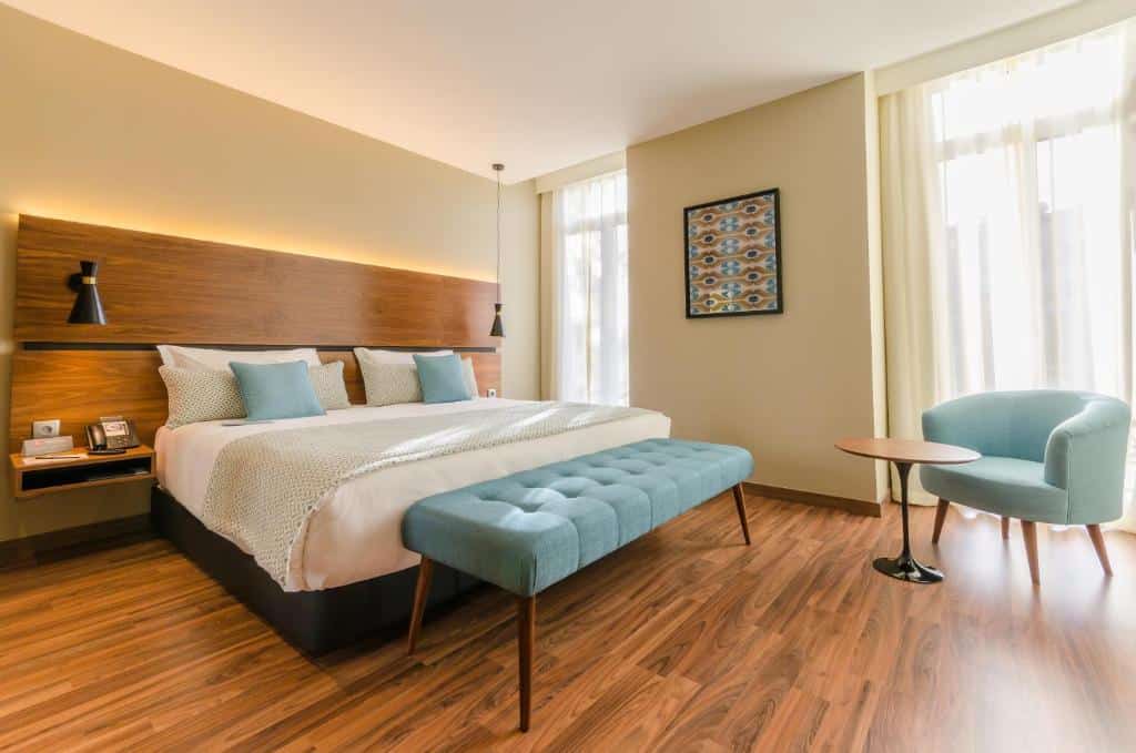 Quarto amplo do Vincci Liberdade com piso que imita madeira, uma cama de casal grande, duas pequenas sacadas com cortinas, há também uma poltrona e um pequena mesinha redonda, para representar hotéis perto da Praça Marquês de Pombal em Lisboa