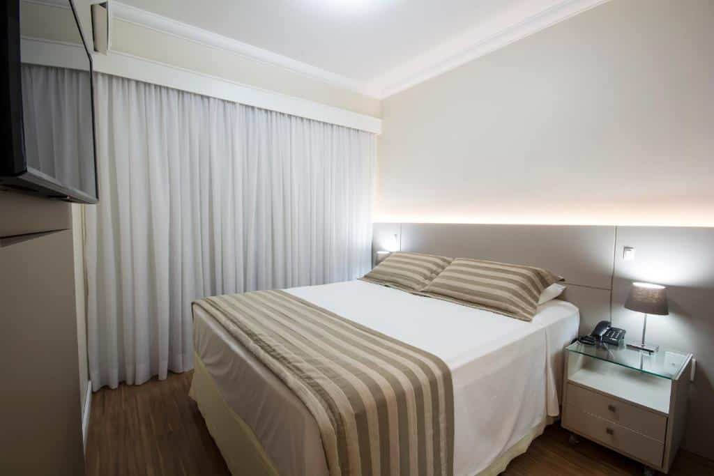 Quarto no Tsue The Palace Flats com uma cama de casal, uma janela com cortinas, uma televisão, chão de madeira e um pequena mesinha de cabeceira com um abajur em cima
