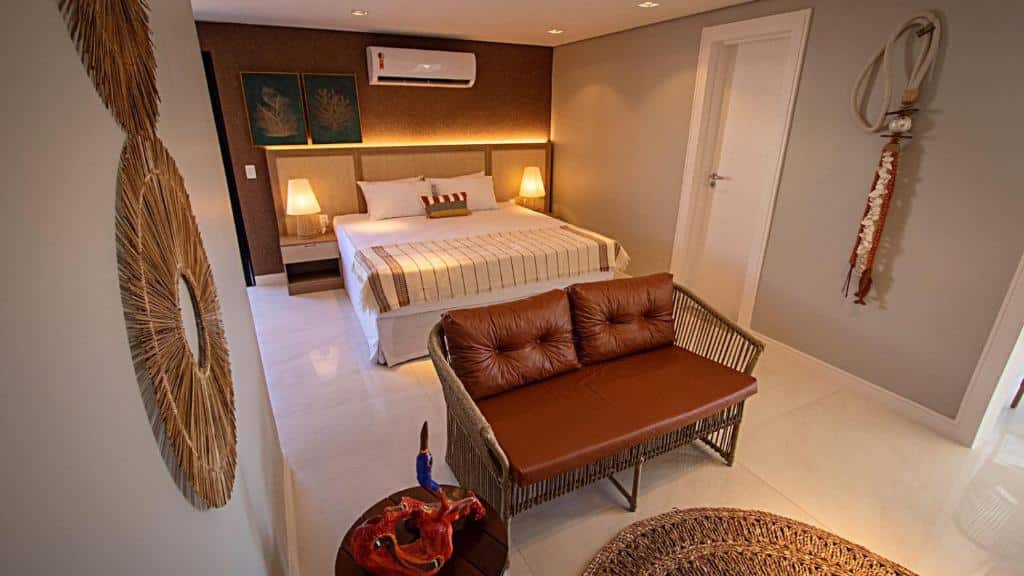 Quarto moderno no Paraiso Beach Hotel com uma cama grande, sofá marrom, mesinhas de cabeceira, luminárias, arte na parede e detalhes decorativos, para representar hotéis perto do Beach Park.