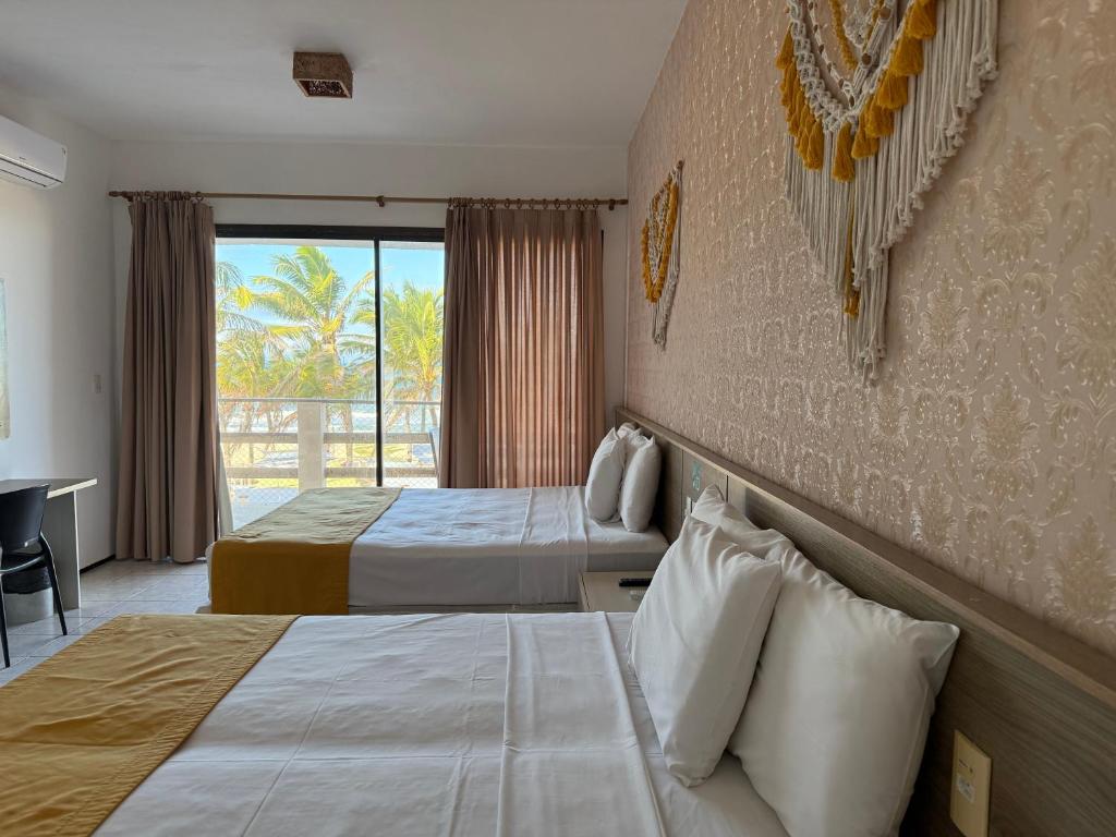 Quarto no Milos Beach Hotel com duas camas de casal, roupa de cama branca, detalhes em amarelo, decoração de parede, escrivaninha e varanda com vista para as palmeiras, para representar hotéis perto do Beach Park.
