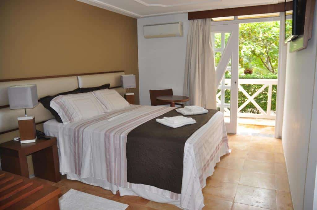 Quarto do Hotel Porto Belo com cama de casal, duas cômodas ao lado, mesa com cadeira do lado esquerdo perto da varanda, para representar hotéis perto do Beach Park.