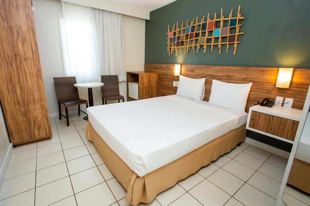 Quarto do Beach Park Hotel – Oceani  com cama de casal, frigobar do lado esquerdo e duas cadeiras e uma mesa, para representar hotéis perto do Beach Park.
