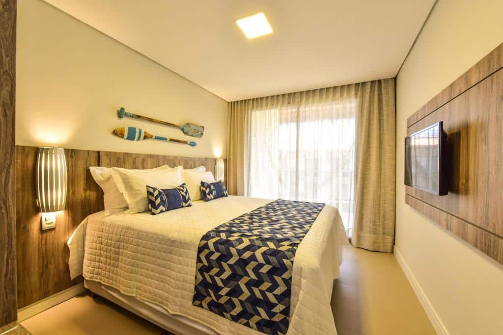 Quarto do Porto das Dunas Praia Hotel com cama de casal, TV em frente a cama, portas de vidro com cortinas brancas que dá acesso a varanda, para representar hotéis perto do Beach Park.