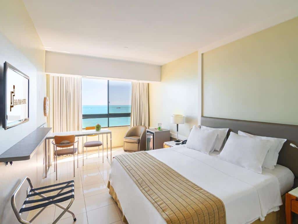 Quarto do Seara Praia Hotel com cama de casal, TV em frente cama, mesa do lado esquerdo perto da janela e poltrona ao lado do frigobar, para representar hotéis perto do Beach Park.