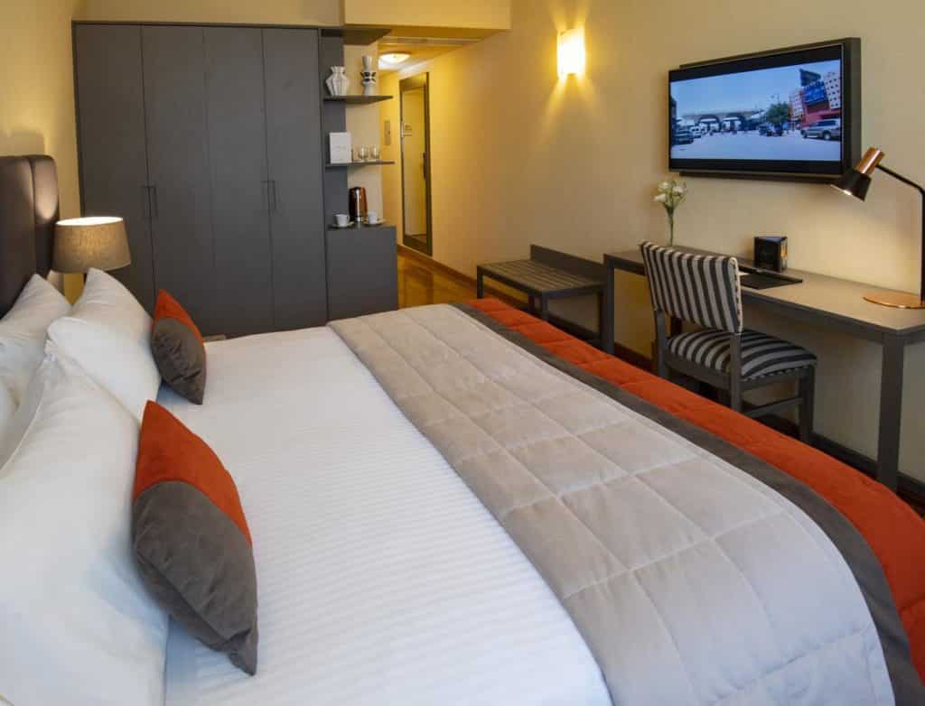 Um quarto no Hotel Grand Brizo Buenos Aires com uma cama bem arrumada, escrivaninha, cadeira, guarda-roupa, TV na parede e uma cafeteria.