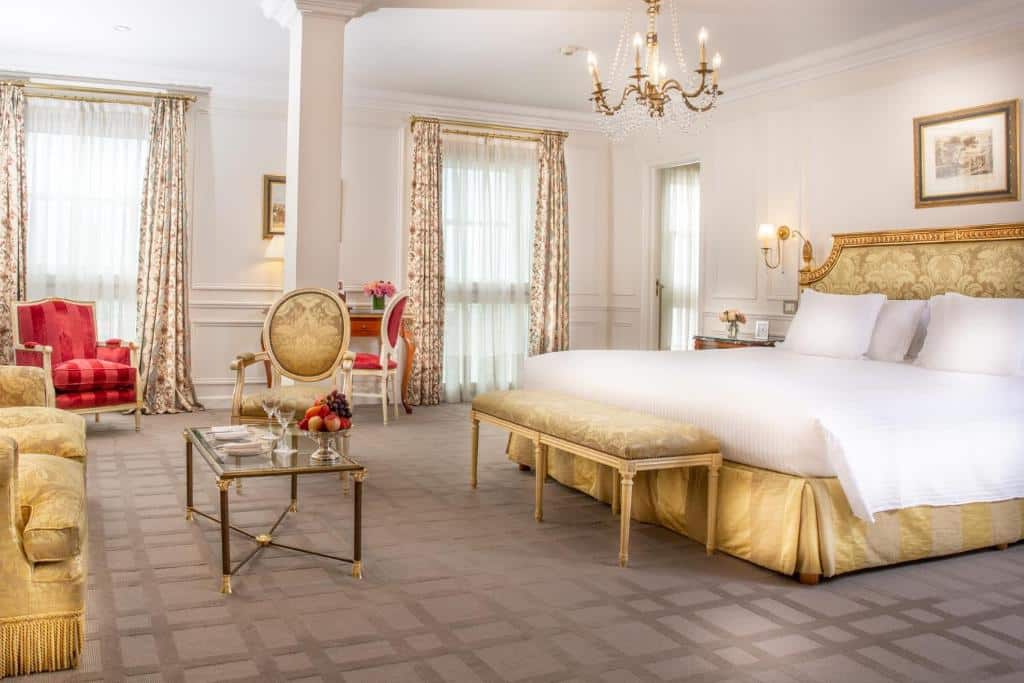 Quarto elegante no Alvear Palace Hotel com uma cama grande, móveis dourados e vermelhos, lustre, poltronas e duas grandes janelas com cortinas, para representar melhores hotéis em Buenos Aires.