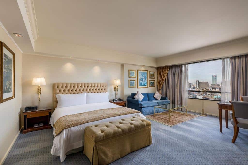 Quarto no Park Tower Hotel Buenos Aires com uma cama grande, sofá azul, mesa de centro de vidro, escrivaninha e vista da cidade por uma janela ampla, para representar melhores hotéis em Buenos Aires.