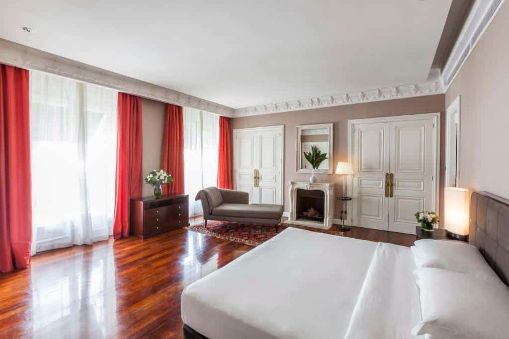 Quarto espaçoso com uma cama branca, piso de madeira, cortinas vermelhas, lareira e elegantes portas duplas brancas, no Palacio Duhau - Park Hyatt Buenos Aires.