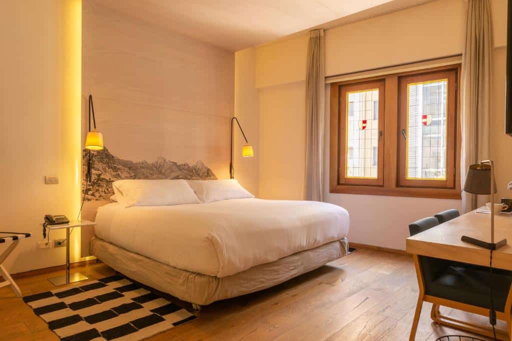 Quarto do Hotel Magnolia com cama de casal, duas luminárias do lado da cama e uma mesa de trabalho com cadeira a frente.