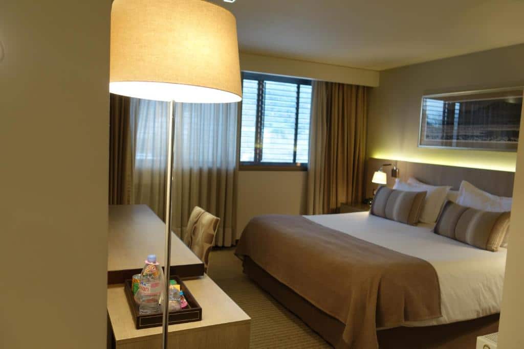 Um quarto do Hotel Los Españoles Plus com uma cama de casal, escrivaninha, abajur, janela com cortinas e garrafa de água na escrivaninha.