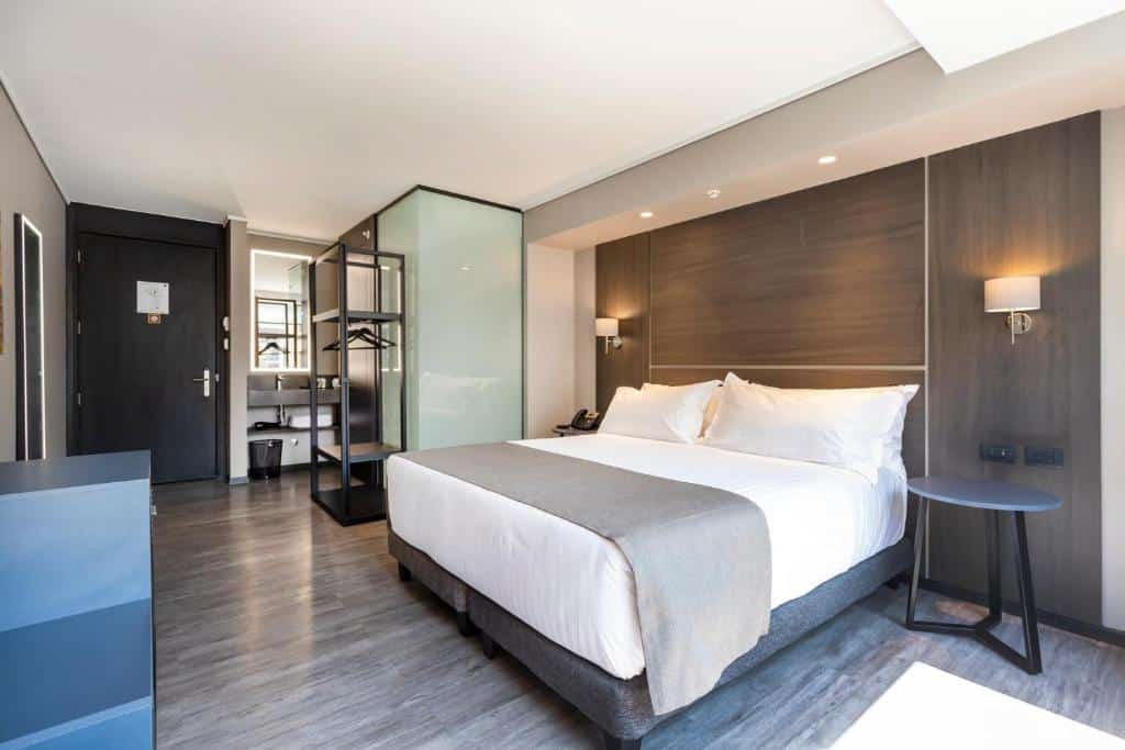 Quarto do Ola Santiago Providencia, Tapestry Collection by Hilton com cama de casal do lado direito com uma mesa redonda ao lado direito da cama do lado esquerdo uma cômoda com telefone.