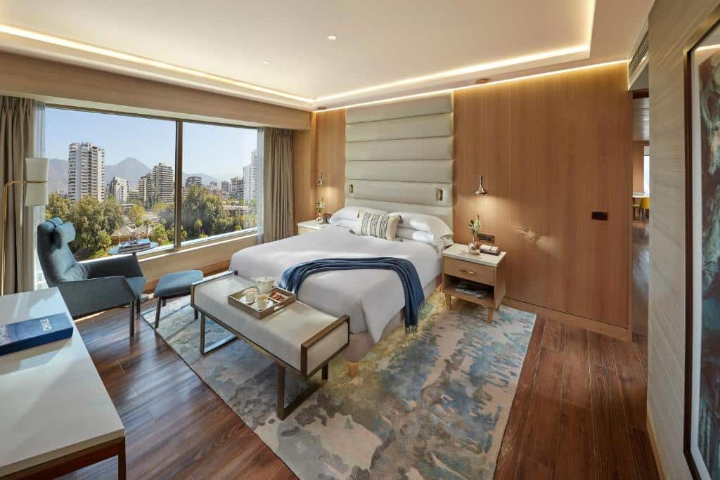 Quarto do Mandarin Oriental, Santiago moderno com cama king-size, janela grande, vista para a cidade, poltrona, escrivaninha e piso de madeira.