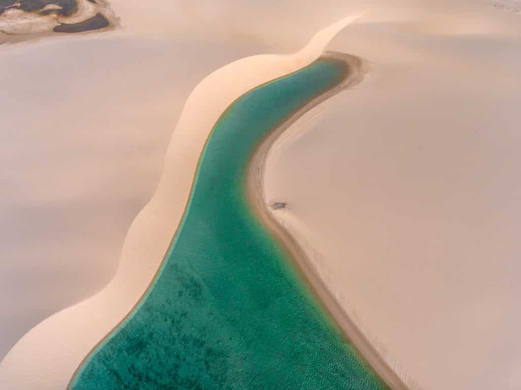 Vista aérea de um sinuoso rio azul-turquesa cercado por suaves dunas de areia bege em uma paisagem desértica.