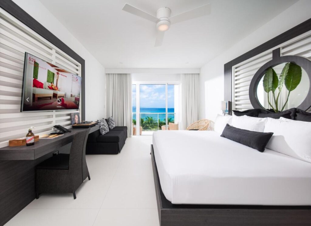 Quarto moderno do S Hotel Montego Bay com cama grande, TV de tela plana, escrivaninha e vista para o mar através de portas de vidro deslizantes.