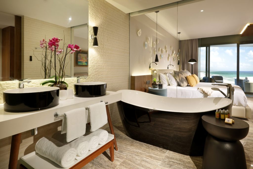 Quarto luxuoso do Grand Palladium Select Costa Mujeres com banheira independente, pias duplas, orquídeas e vista para o mar através de grandes janelas.
