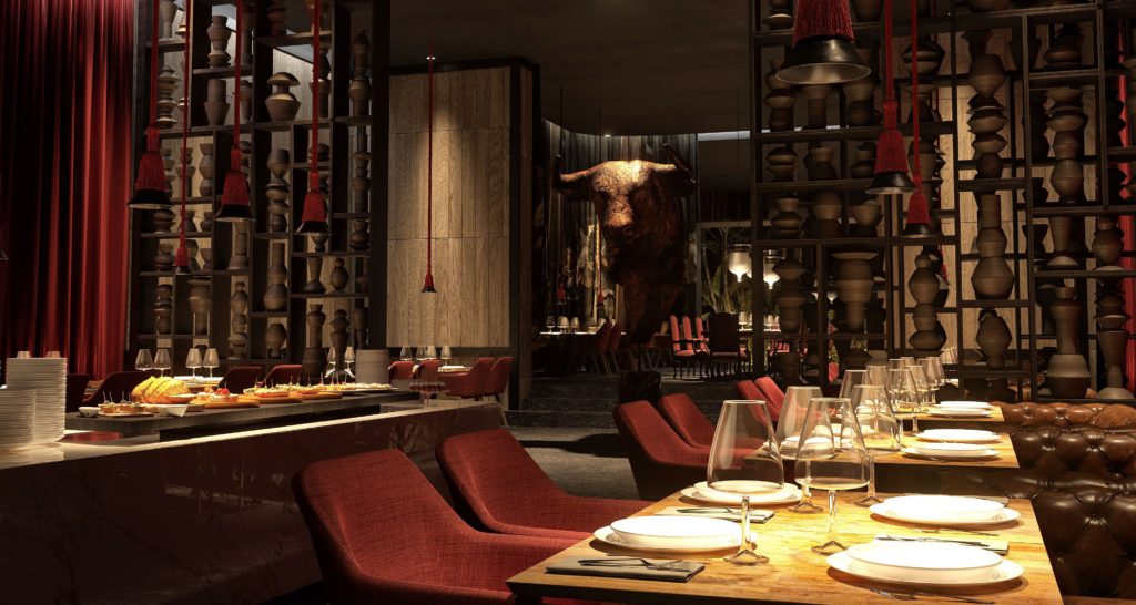 Um restaurante com pouca iluminação no Grand Palladium Select Costa Mujeres apresenta cadeiras vermelhas, mesas postas e cerâmica decorativa nas prateleiras, com uma grande escultura de touro ao fundo. Esse é um dos melhores resorts all inclusive no Caribe.
